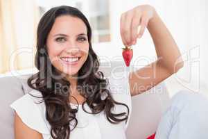 Pretty brunette eating strawberries on couch