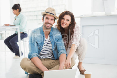 Happy colleagues sitting on the floor using laptop