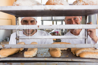 Smiling bakers looking through tray of bread