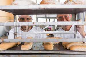 Smiling bakers looking through tray of bread
