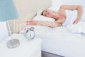 Blonde woman lying in bed reaching for alarm clock