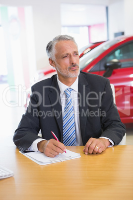 Focused salesman writing on clipboard at his desk