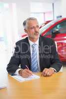 Focused salesman writing on clipboard at his desk