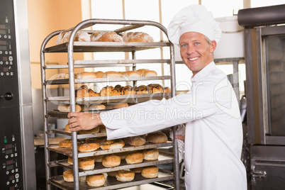 Smiling baker pushing tray of bread