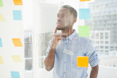 Thoughtful businessman looking at sticky notes on window