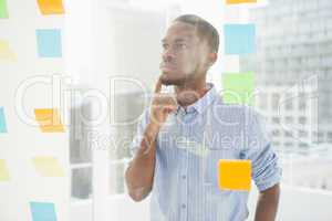 Thoughtful businessman looking at sticky notes on window