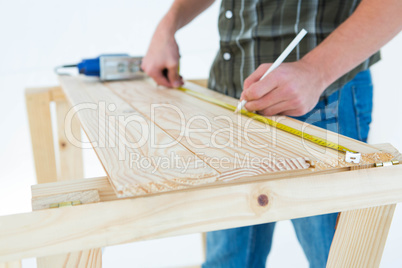 Carpenter marking with measure tape on wooden plank