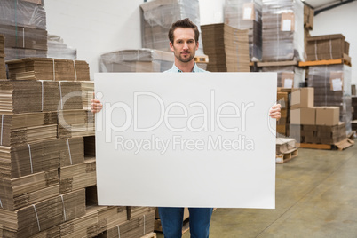 Smiling warehouse worker holding large white poster