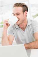 Cheerful businessman using laptop while drinking