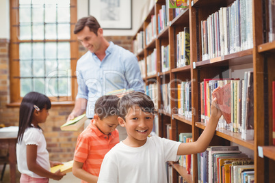 Cute pupils and teacher looking for books in library