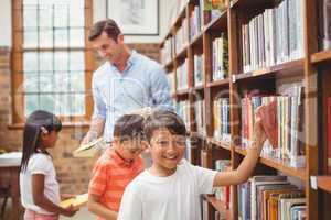 Cute pupils and teacher looking for books in library