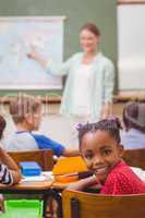 Cute pupil smiling at camera at his desk in classroom