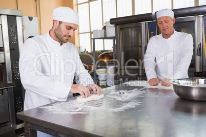 Focused bakers kneading dough at counter