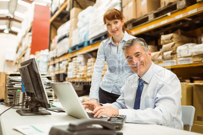 Warehouse management talking and looking at laptop