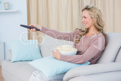 Smiling blonde changing tv channel while eating popcorn