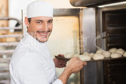 Smiling baker putting dough in oven