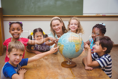 Cute pupils and teacher in classroom with globe