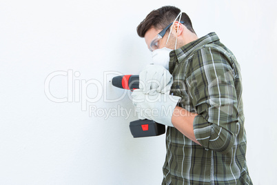 Carpenter using drill machine on white wall