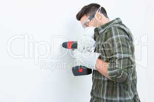 Carpenter using drill machine on white wall