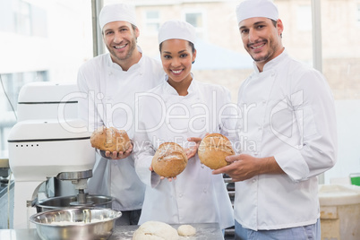Team of bakers smiling at camera holding bread