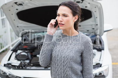 Annoyed woman on the phone beside her broken down car