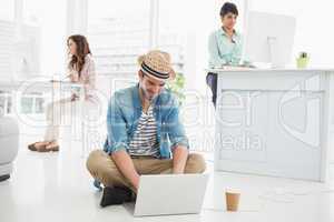 Happy businessman sitting on the floor using laptop
