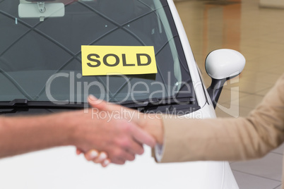 Person shaking hands in front of a sold car