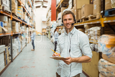 Warehouse manager wearing headset writing on clipboard Warehouse manager wearing headset writing on clipboard