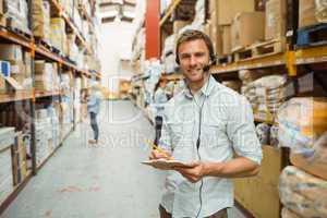 Warehouse manager wearing headset writing on clipboard