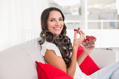 Pretty brunette eating strawberries on couch