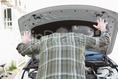 Angry man checking his car engine after breaking down