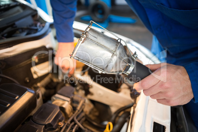 Mechanic examining under hood of car with torch