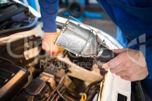 Mechanic examining under hood of car with torch