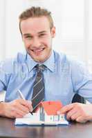 Smiling businessman taking notes and holding miniature home