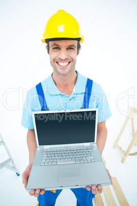 Happy repairman wearing hard hat while holding laptop