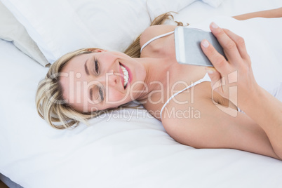 Smiling blonde woman lying in bed text messaging