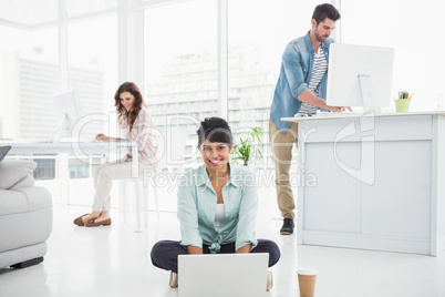 Smiling businesswoman sitting on the floor using laptop