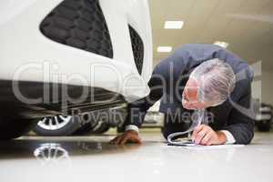 Businessman looking under the car while writing on clipboard