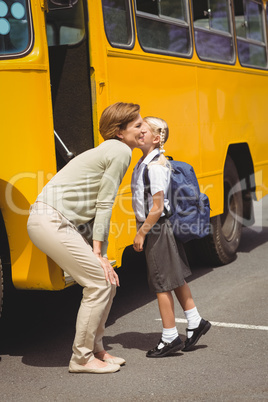 Mother kissing her daughter by school bus