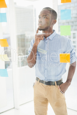 Thoughtful businessman looking at sticky notes on window