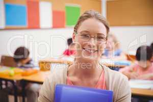 Pretty teacher smiling at camera while holding folder