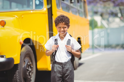 Cute pupil smiling at camera by the school bus