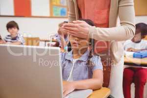 Teacher covering pupil eyes in front of the computer
