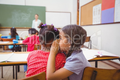 Cute pupils whispering in classroom