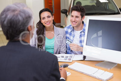 Smiling couple holding credit card to buy a car