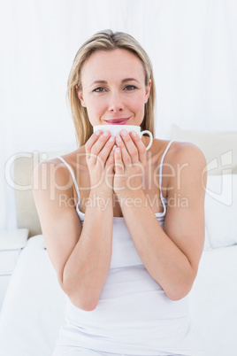 Smiling blond sitting on bed holding mug