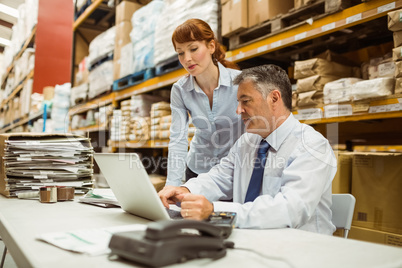 Warehouse management talking and looking at laptop