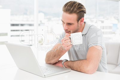 Focused businessman holding cup while using laptop