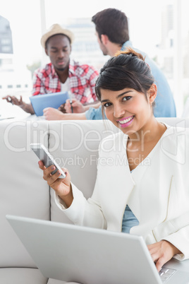 Smiling businesswoman using mobile and laptop on couch