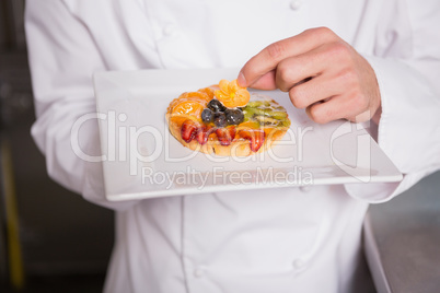 Close up of baker putting flower on the pastry with fruit